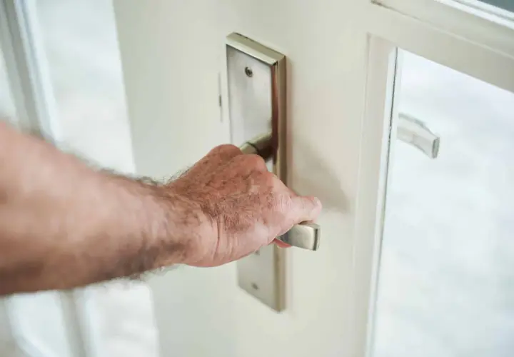 Main d'homme saisissant la poignée d'une porte blanche, prête à en modifier le sens d'ouverture.