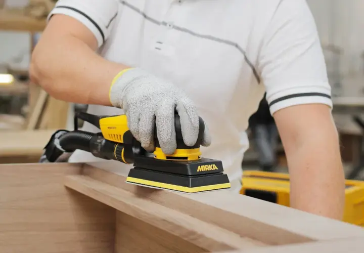 Un artisan utilise une ponceuse pour porte en bois, préparant une surface lisse pour un projet de menuiserie.