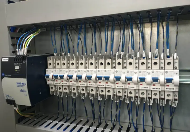 Panneau électrique avec alimentation Allen-Bradley et disjoncteurs. Le code couleur des câbles électriques est visible, indiquant leur section et leur destination.