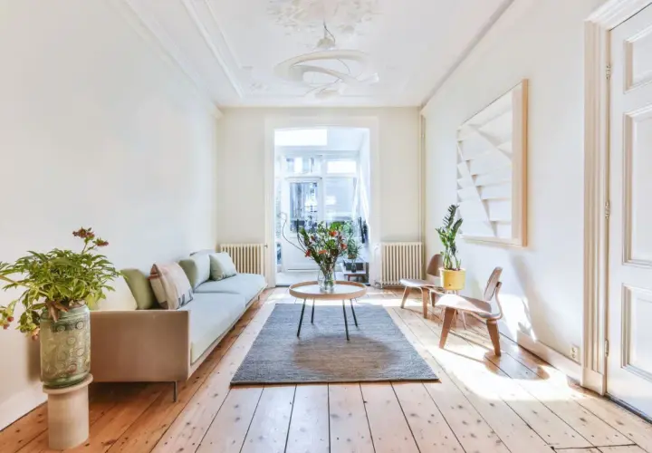 Salon lumineux avec parquet clair, canapé, table basse et bouquet de fleurs. Le parquet semble avoir été traité pour blanchir le bois.