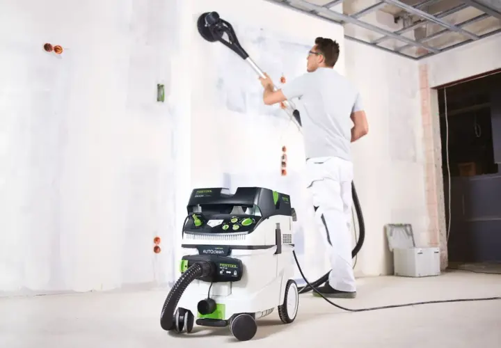 Un ouvrier utilise un aspirateur pour girafe afin de poncer un mur.