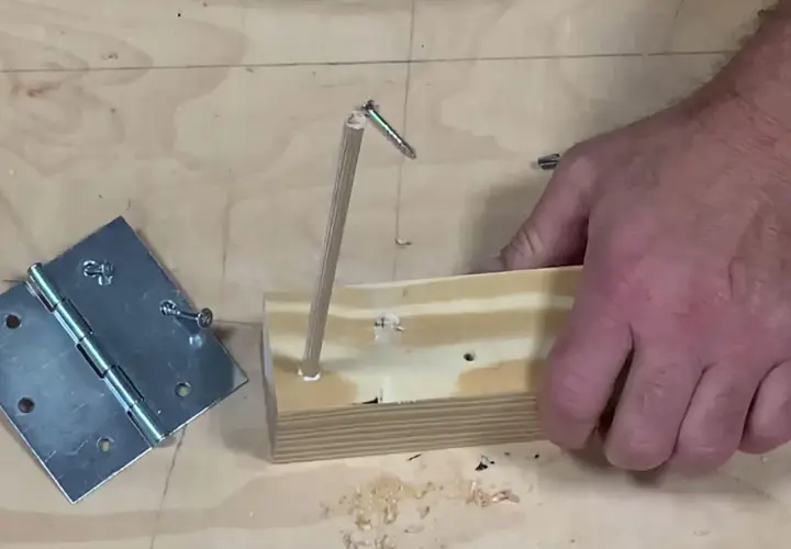 Un bricoleur teste un montage : une vis qui tourne dans le vide, tenue par un bout de bois, à côté d'une charnière.