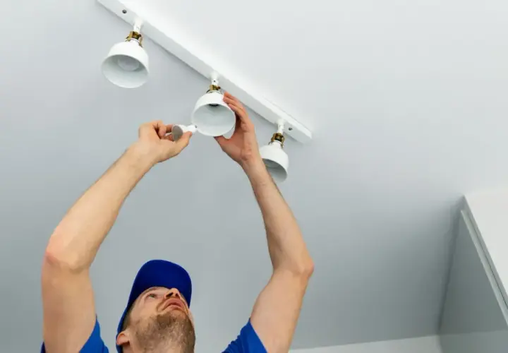 Un électricien installe des spots sur un rail. Il est important de savoir combien de spot par disjoncteur pour une installation sûre.