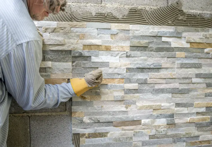 Pose de pierre de parement intérieur, un artisan ajuste une pierre sur un mur en cours de finition.
