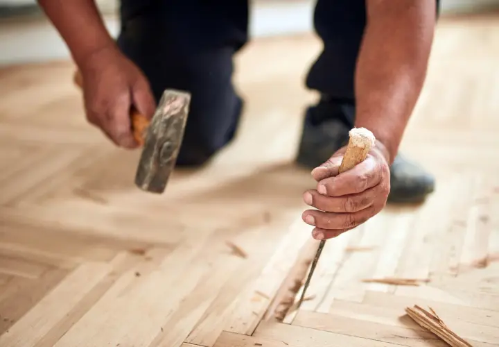 Un artisan utilise un ciseau et un marteau pour changer une lame de parquet flottant endommagée.