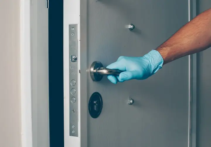 Main tenant, ganté, ouvre une porte voilée.