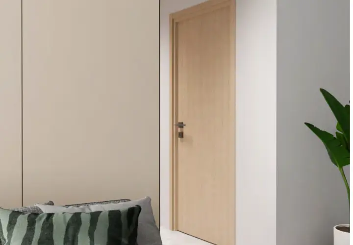 Une porte en bois clair, d'une largeur standard, s'ouvre sur un couloir. Des coussins décoratifs sont posés sur un canapé à gauche.
