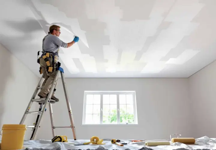 Un peintre sur une échelle pose une toile de verre au plafond.