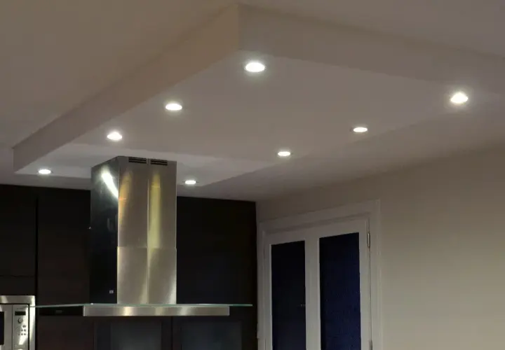 Un caisson plafond avec spots éclaire une cuisine moderne. La hotte en inox et les meubles sombres créent un contraste élégant.