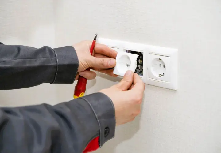 Un électricien installe une prise, prêt à condamner une prise électrique défectueuse.