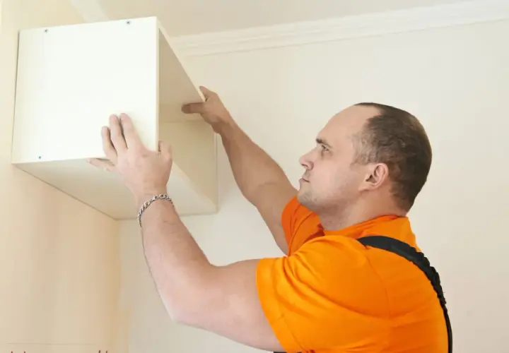 Un homme en t-shirt orange est en train de fixer un caisson blanc au mur.