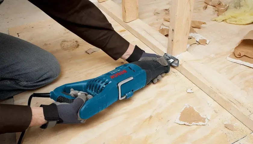 Une scie sabre sert à découper le bois et le métal, comme le montre cette personne qui l'utilise pour démolir une structure.