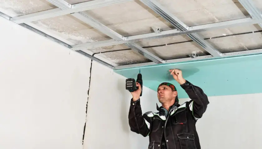Un ouvrier installe une plaque de plâtre sur une structure métallique pour créer un faux plafond placo.