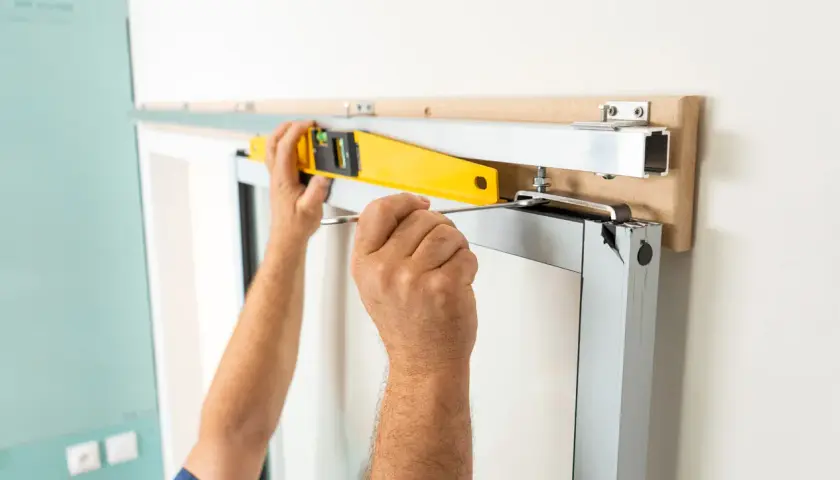 Pose en applique porte : un ouvrier ajuste un rail avec un niveau à bulle et un tournevis pour une installation parfaite.
