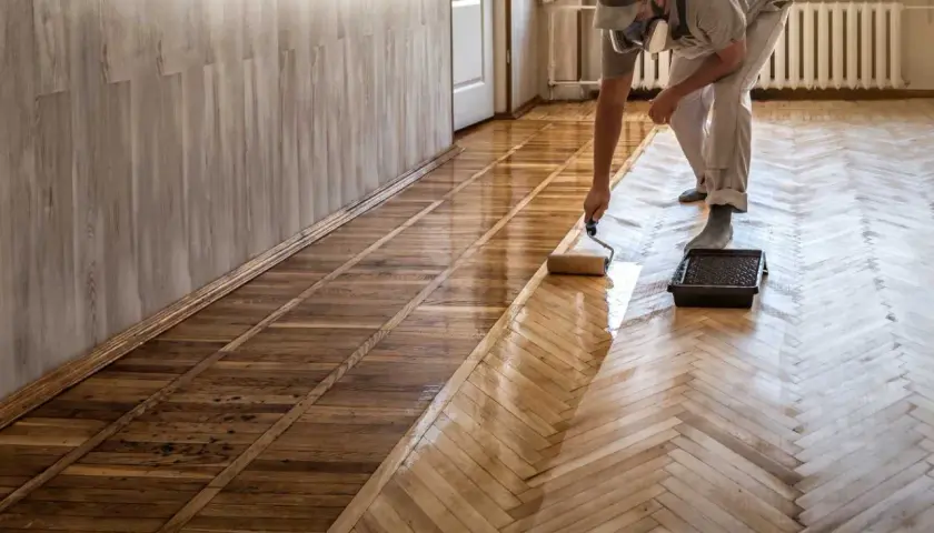 Pose de carrelage imitation parquet : un professionnel applique une couche protectrice sur un sol en chevrons.