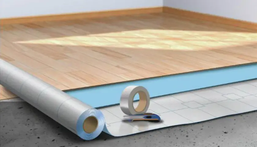 Préparation pour la pose sous couche parquet : rouleau isolant, ruban adhésif et cutter sur un sol brut.