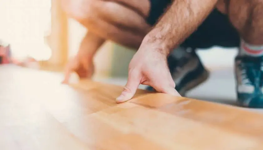 Un homme s'accroupit pour faire un plancher bois, posant délicatement une lame de parquet.