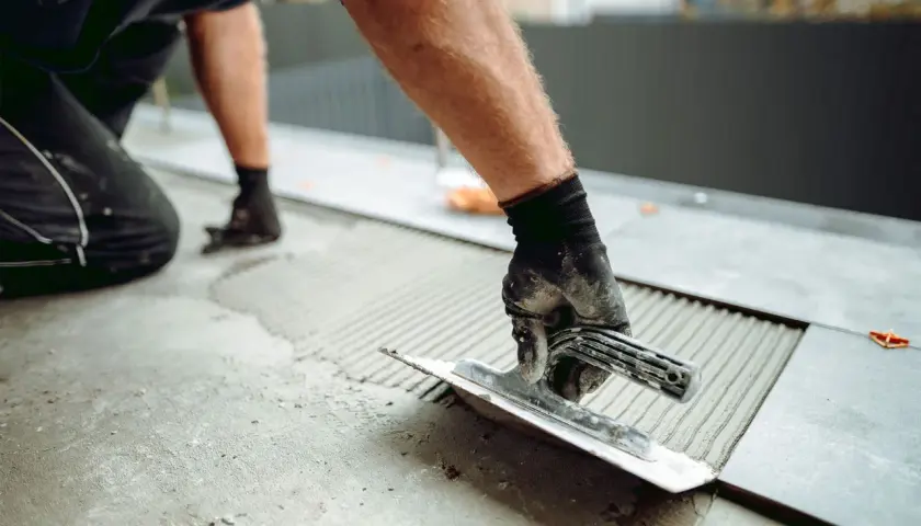 Un carreleur utilise une truelle pour étaler du mortier, un élément essentiel de l'outillage du carreleur, avant de poser une nouvelle dalle.
