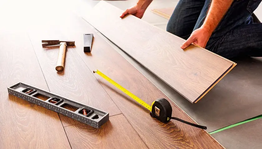 Pose d'un coupe parquet flottant. Outils de pose : niveau, marteau, mètre ruban.