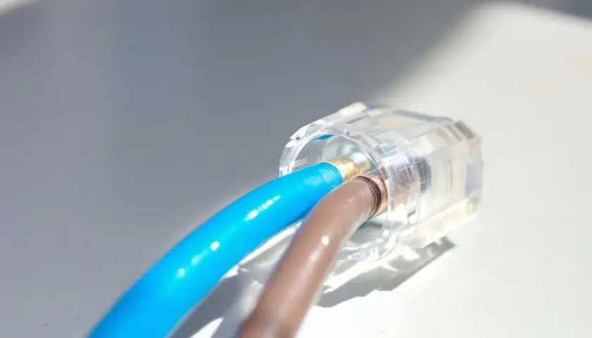 Connexion électrique sécurisée : deux fils, un bleu et un marron, sont raccordés sans domino dans un connecteur transparent.