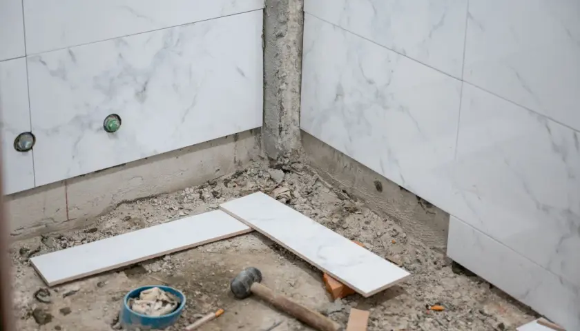 Travaux de salle de bain : pose de carreaux sur du carrelage existant. Marteau, briques et carreaux blancs sont prêts pour le chantier.