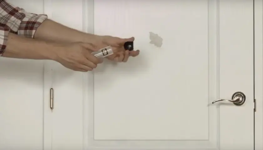Un homme montre comment réparer un trou dans une porte avec un kit de réparation.