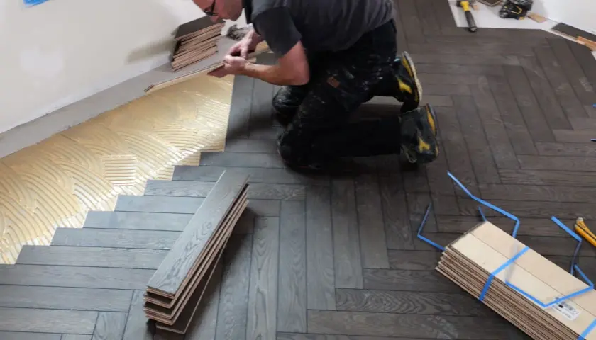 Pose de parquet en pose bâton rompu. Un artisan applique de la colle sur le sol avant de poser les lames de bois.