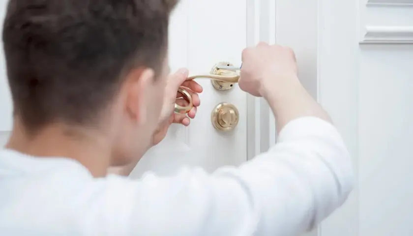 Un homme tente de débloquer une poignée de porte dorée. Le carré de porte bloqué résiste.