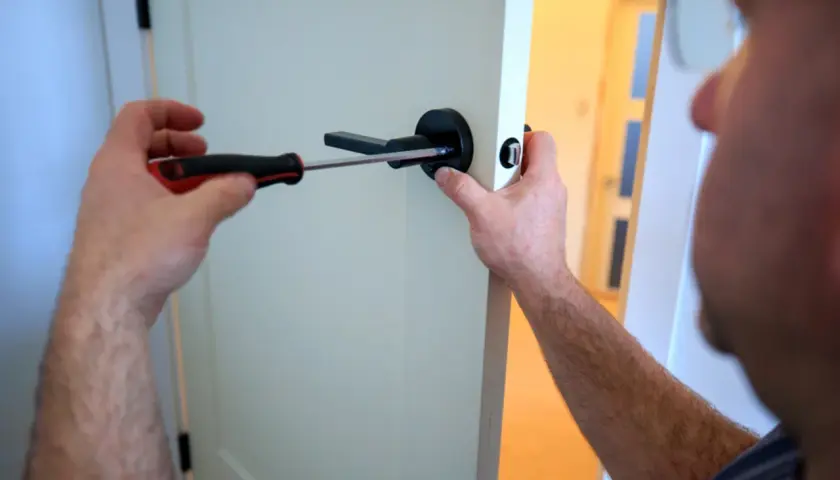 Un homme utilise un tournevis pour changer la poignée de porte.