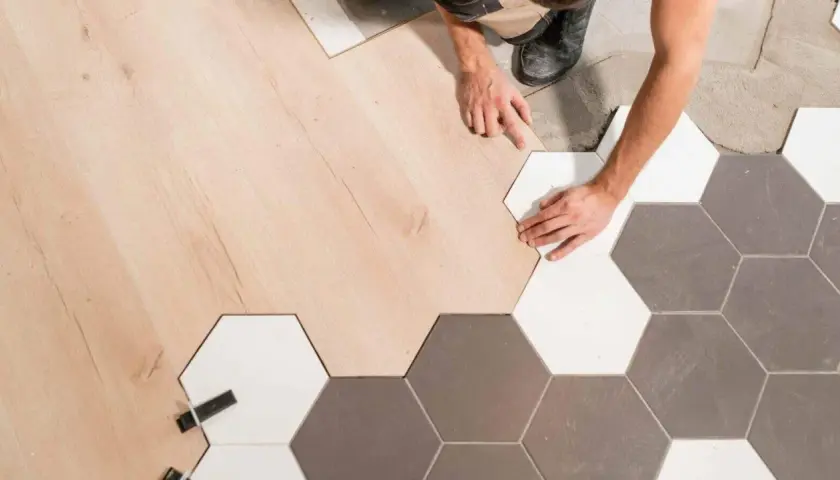 Pose d'un parquet en bois clair à la jonction avec un carrelage hexagonal gris et blanc.