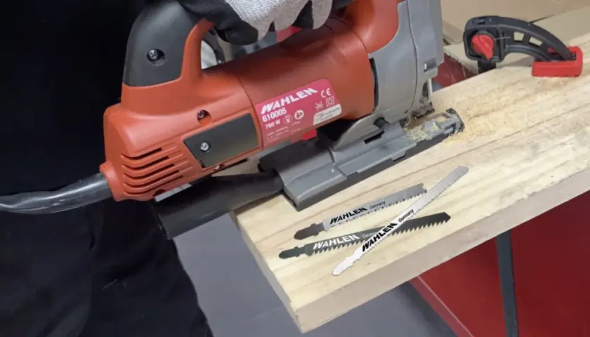 Un bricoleur utilise une scie sauteuse, un type de scie, pour travailler du bois. Trois lames de scie sont visibles.