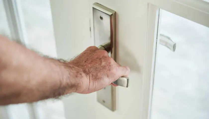 Main d'homme saisissant la poignée d'une porte blanche, prête à en modifier le sens d'ouverture.