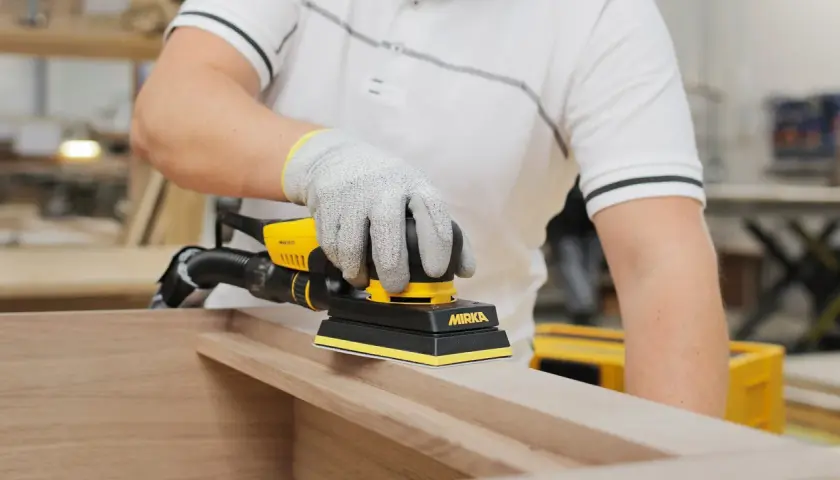 Un artisan utilise une ponceuse pour porte en bois, préparant une surface lisse pour un projet de menuiserie.