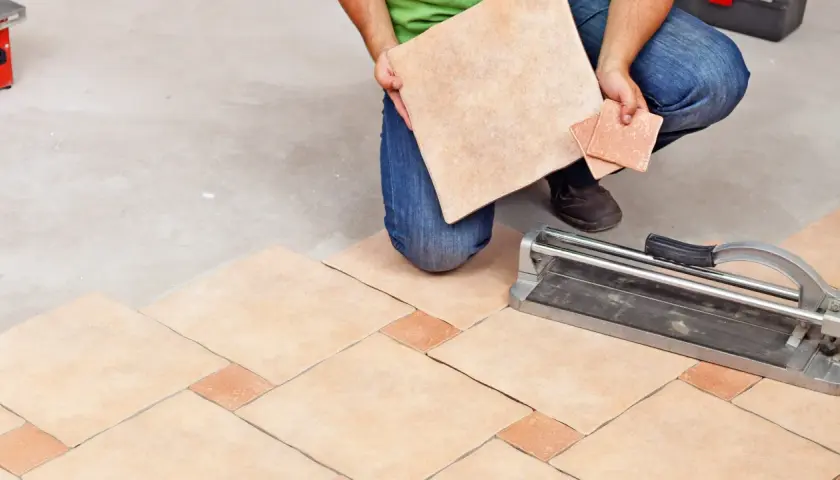 Un carreleur prépare la découpe de carrelage pour un nouveau sol. L'outil de coupe est prêt.