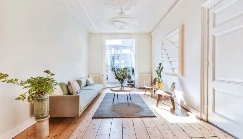 Salon lumineux avec parquet clair, canapé, table basse et bouquet de fleurs. Le parquet semble avoir été traité pour blanchir le bois.