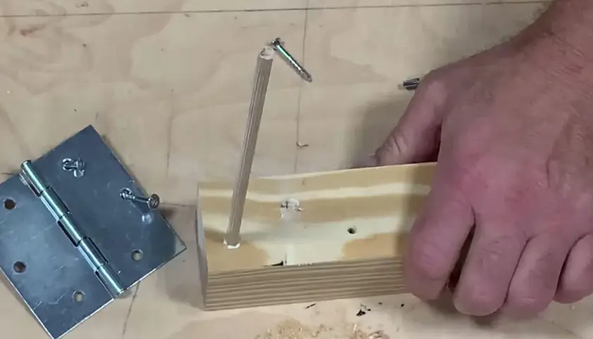 Un bricoleur teste un montage : une vis qui tourne dans le vide, tenue par un bout de bois, à côté d'une charnière.