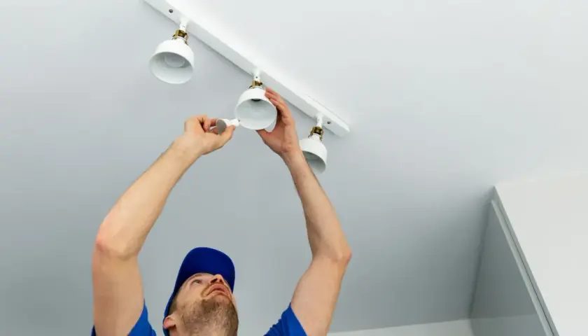 Un électricien installe des spots sur un rail. Il est important de savoir combien de spot par disjoncteur pour une installation sûre.