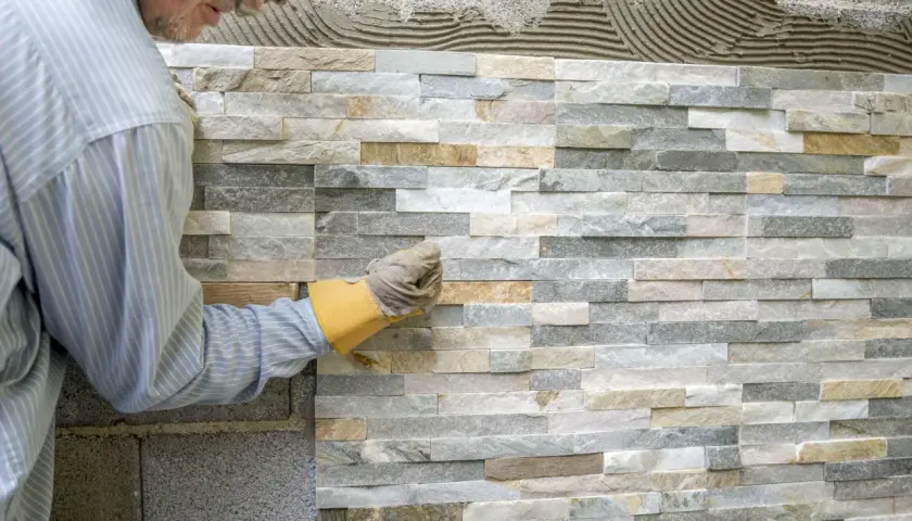 Pose de pierre de parement intérieur, un artisan ajuste une pierre sur un mur en cours de finition.