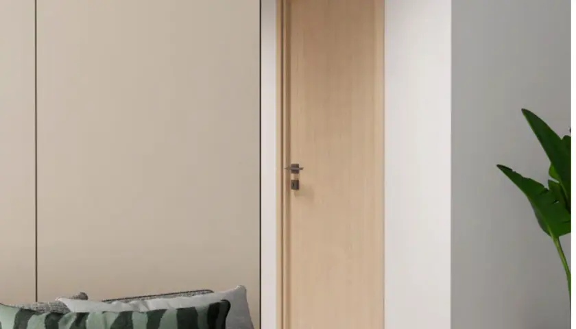 Une porte en bois clair, d'une largeur standard, s'ouvre sur un couloir. Des coussins décoratifs sont posés sur un canapé à gauche.