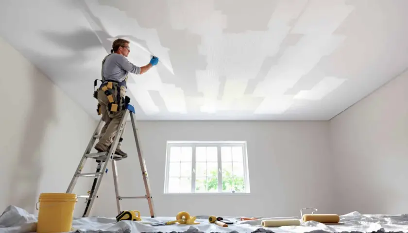 Un peintre sur une échelle pose une toile de verre au plafond.