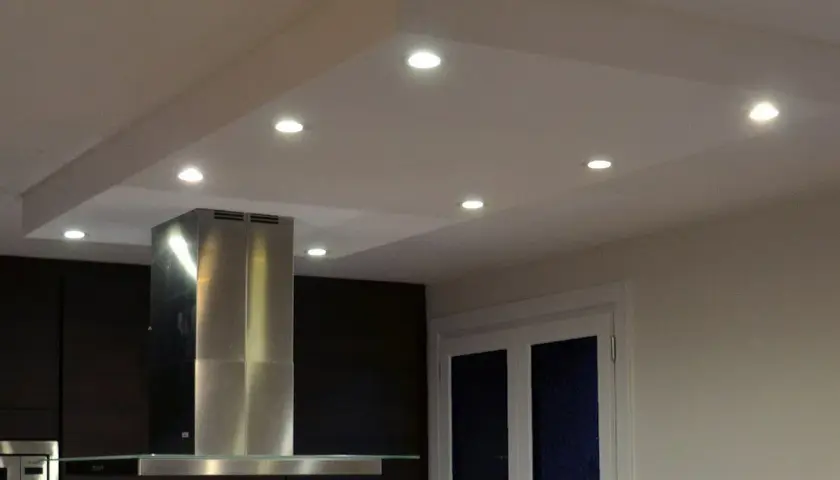 Un caisson plafond avec spots éclaire une cuisine moderne. La hotte en inox et les meubles sombres créent un contraste élégant.