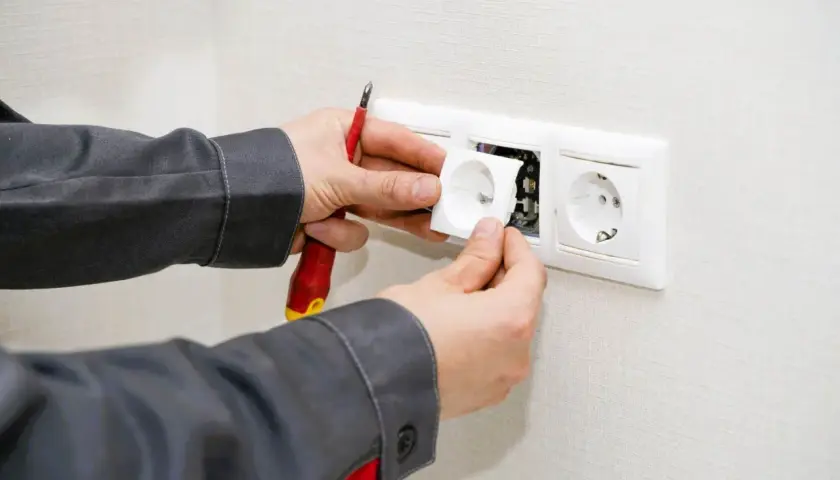 Un électricien installe une prise, prêt à condamner une prise électrique défectueuse.