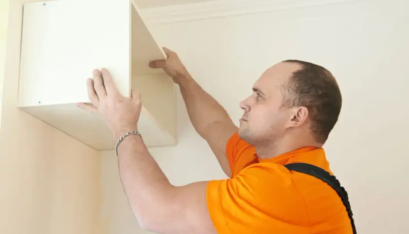 Un homme en t-shirt orange est en train de fixer un caisson blanc au mur.
