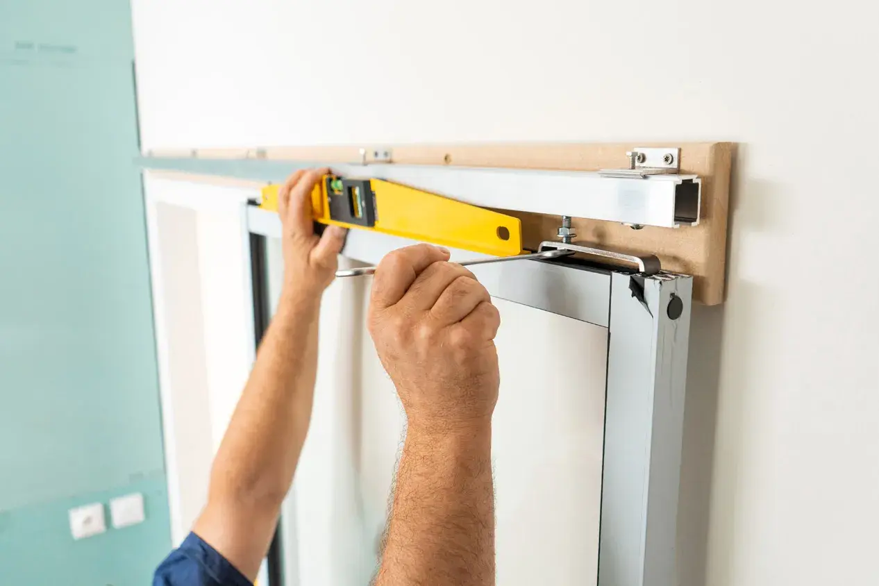 Pose en applique porte : un ouvrier ajuste un rail avec un niveau à bulle et un tournevis pour une installation parfaite.