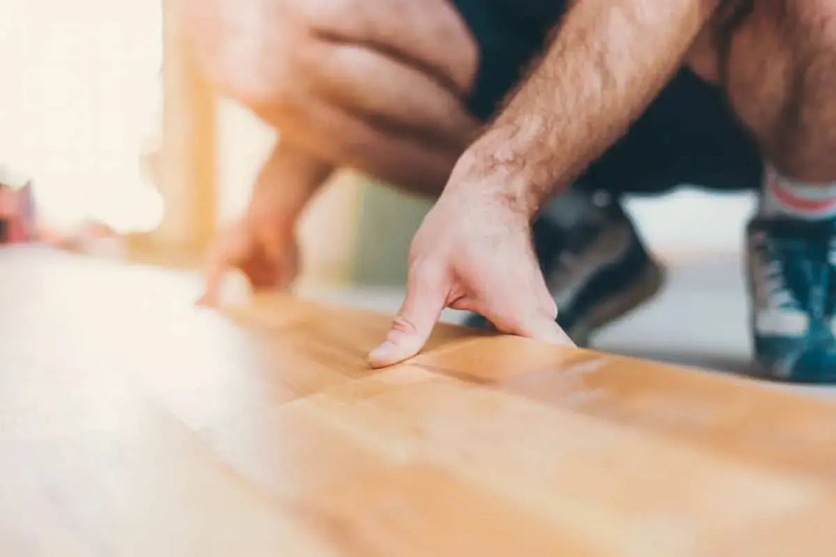 Un homme s'accroupit pour faire un plancher bois, posant délicatement une lame de parquet.