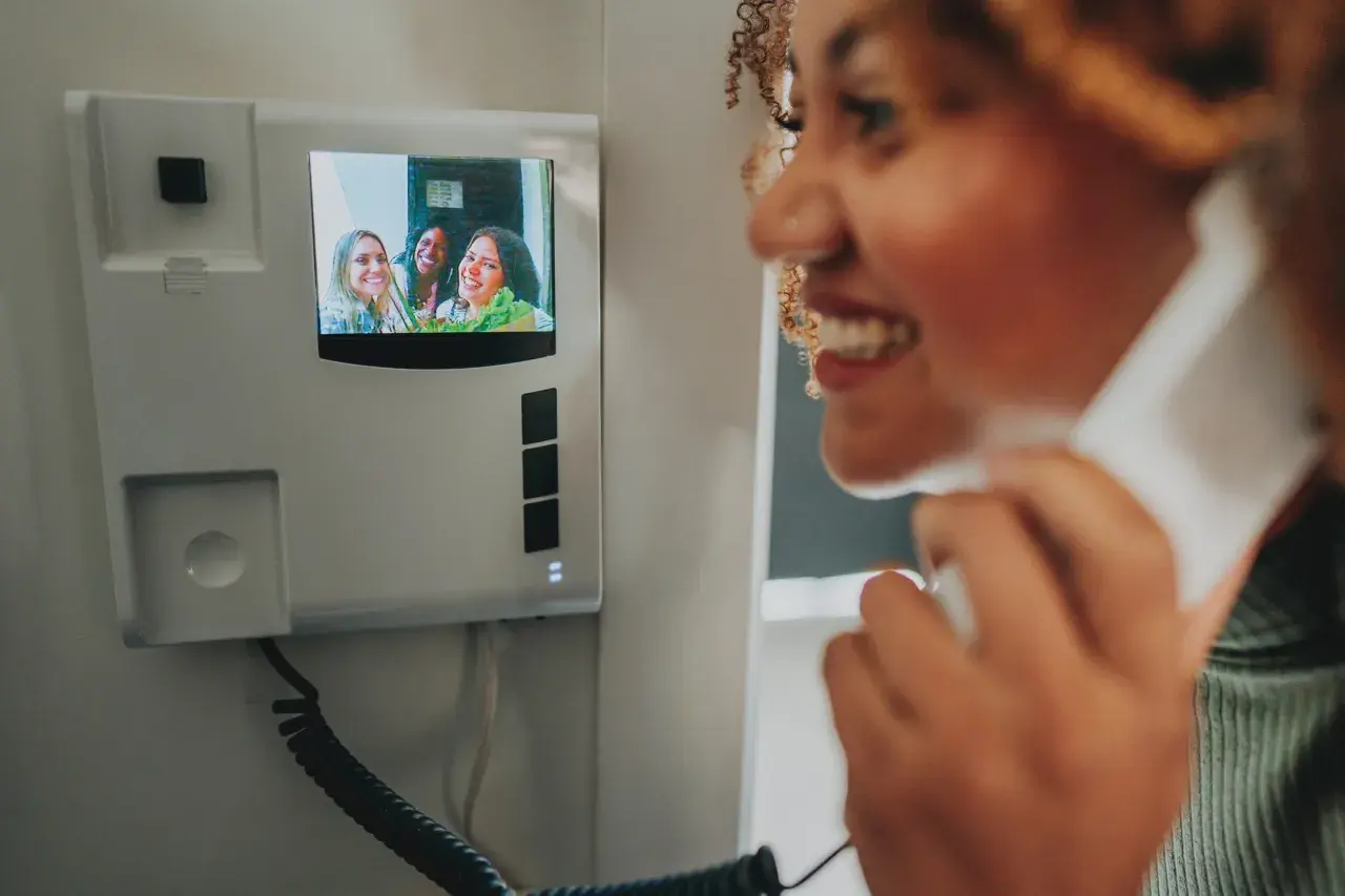 Une femme souriante utilise un visiophone pour parler à des amies. L'installation du visiophone est simple et moderne.