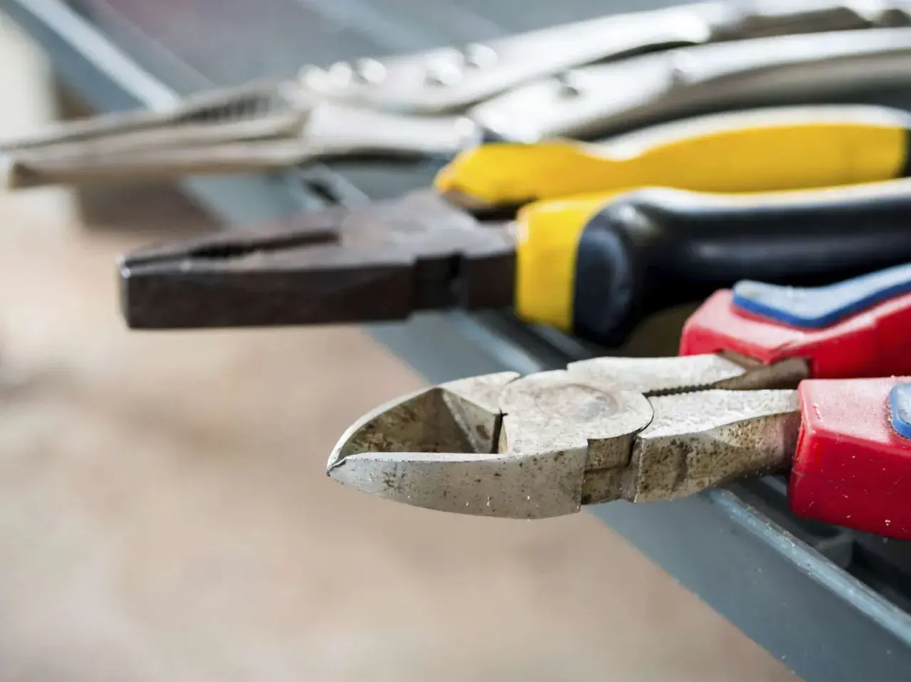 Divers types de pinces bricolage, dont une pince coupante et une pince universelle, sont alignées sur une surface grise.
