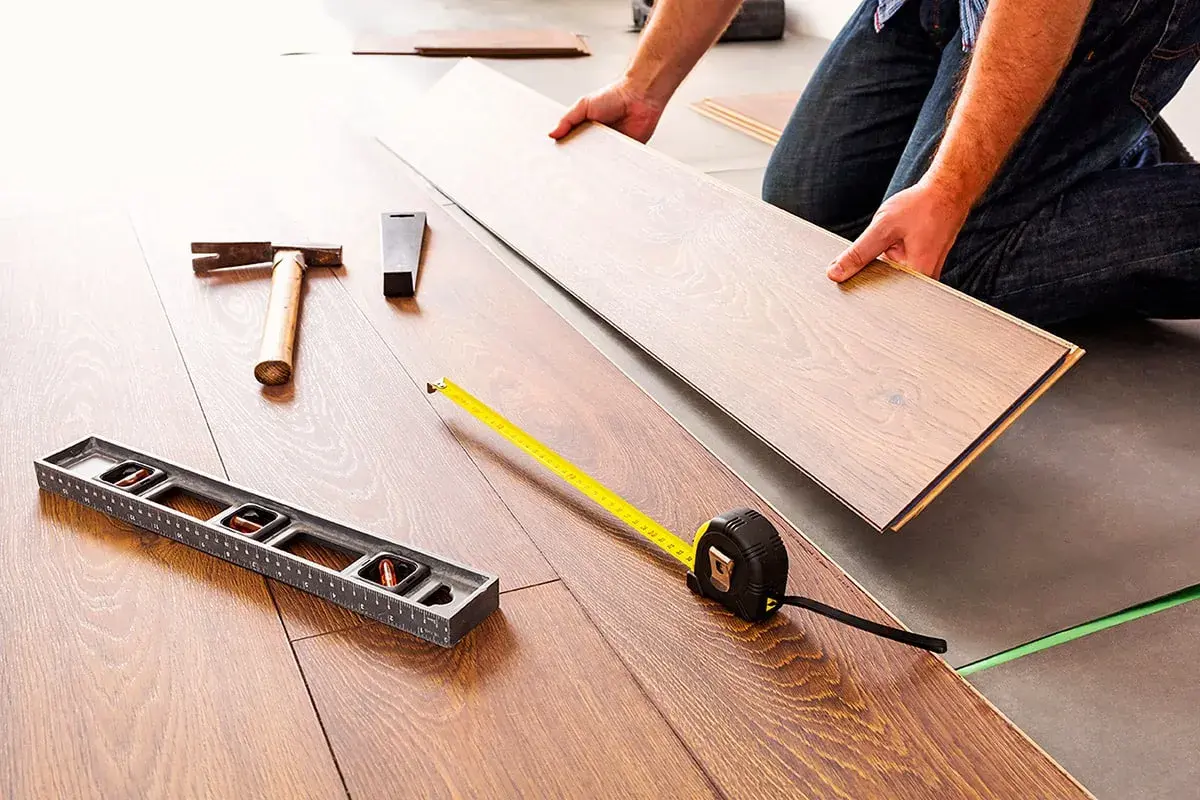 Pose d'un coupe parquet flottant. Outils de pose : niveau, marteau, mètre ruban.