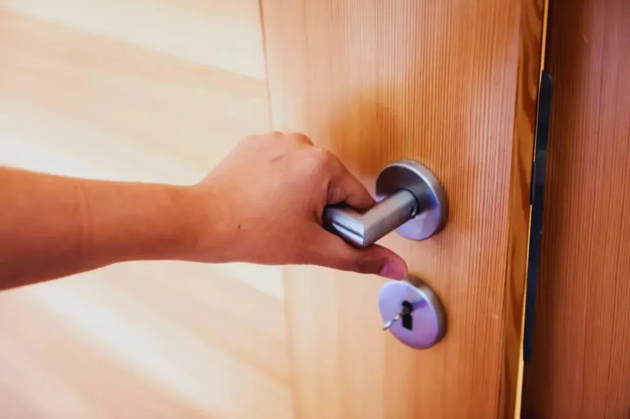 Main tenant essaie de fermer une porte qui ne ferme plus, la poignée est bloquée.