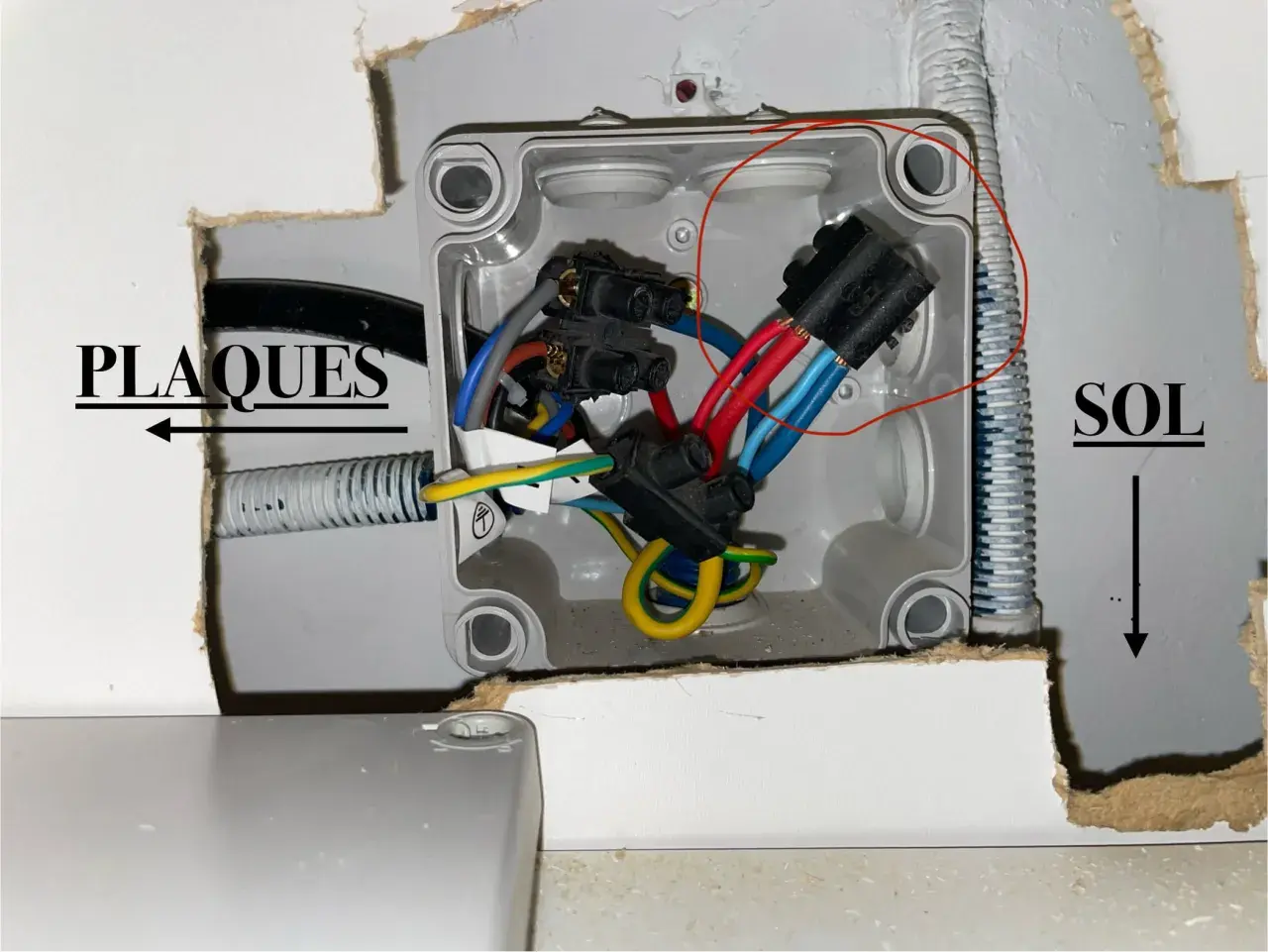 Boîtier électrique ouvert avec fils rouges, bleus et jaunes. Une prise male pour four est visible, connectée à des fils.